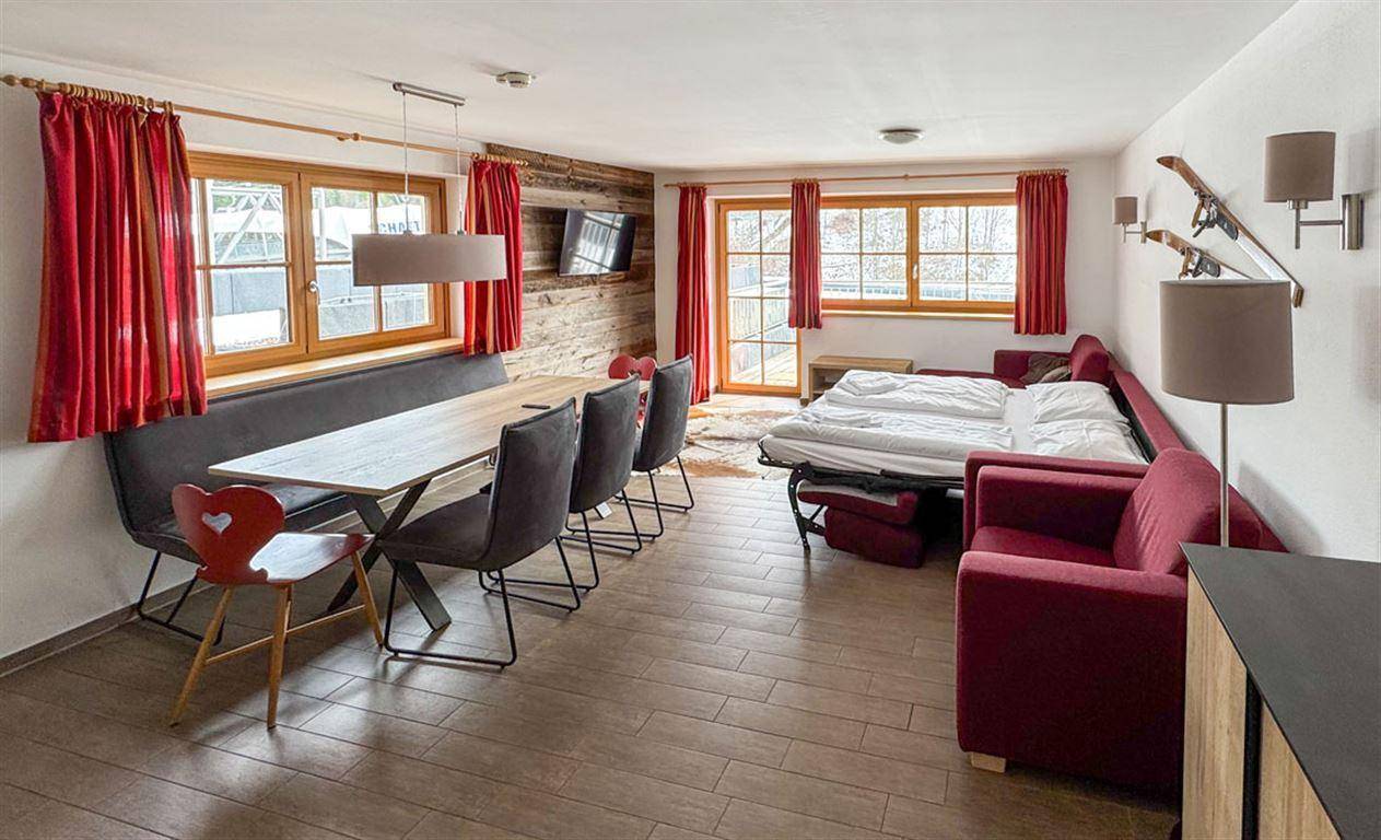 Gemütlicher Wohn-Essbereich im alpinen Stil mit Schlafsofa, Esstisch und Holzwand.