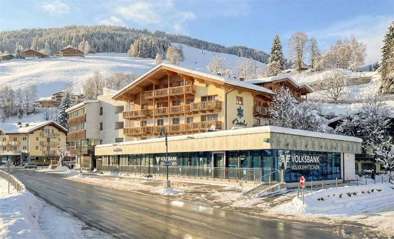 Alpines Gebäude mit Holzbalkonen und einer Bankfiliale im Erdgeschoss, umgeben von Schnee.