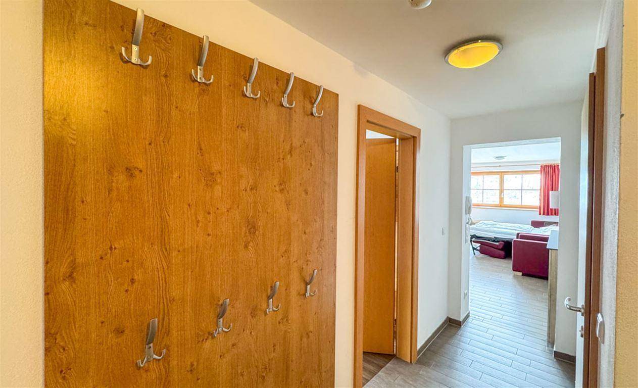 Heller Flur mit Holzwandverkleidung und Garderobenhaken, führt in den Wohnbereich.