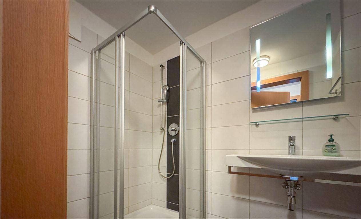Modernes Badezimmer mit Duschkabine, Waschbecken und hellen Fliesen an den Wänden.