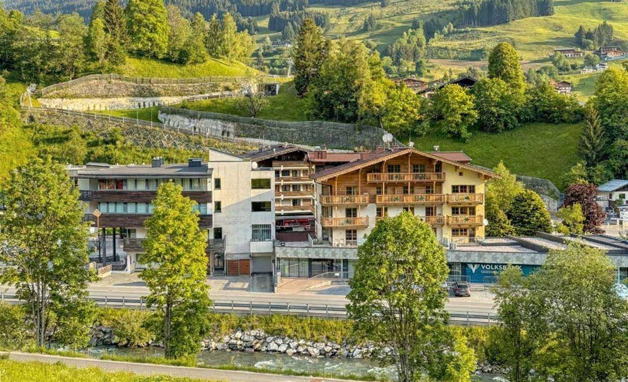 Alpines Gebäude mit Holzbalkonen und grüner Umgebung im Sommer, neben einem Fluss.