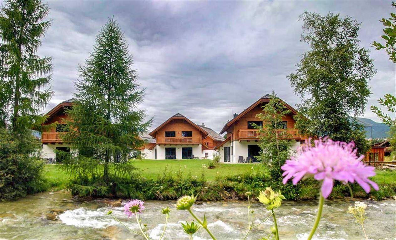 Ferienhäuser in grüner Landschaft am Flussufer mit blühenden Blumen im Vordergrund.