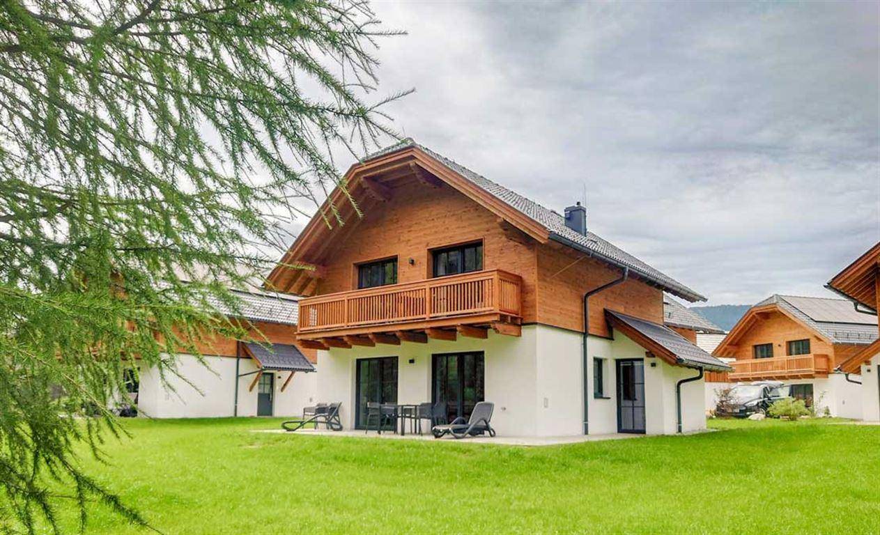 Modernes Holzhaus mit großer Rasenfläche und Terrasse mit Gartenmöbeln.