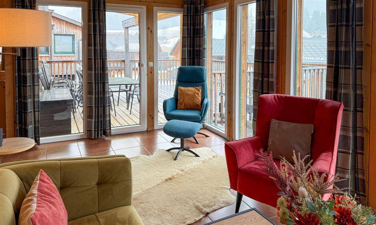 Wohnzimmer mit bequemen Sesseln und Blick auf die Außenterrasse mit Sitzgelegenheiten.