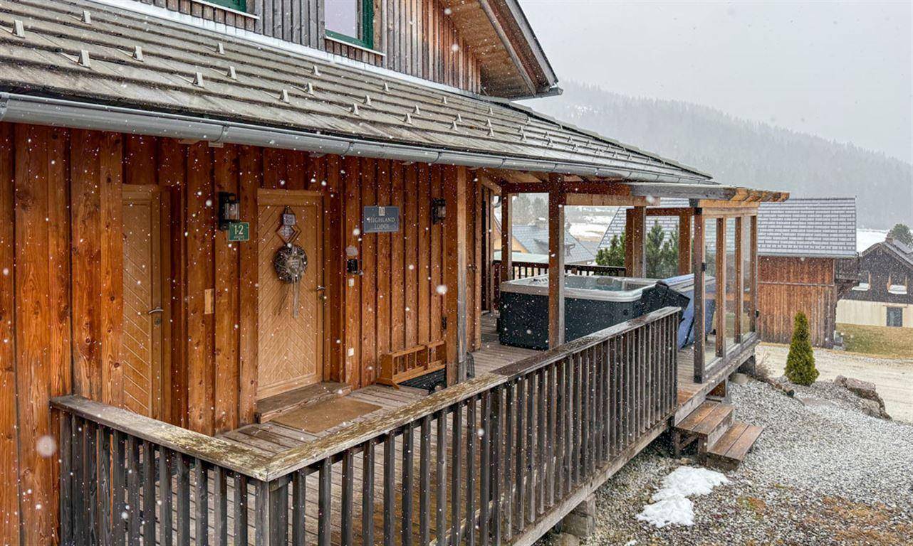 Eingangsbereich eines Holzhauses mit Whirlpool auf der Terrasse im winterlichen Schneetreiben.