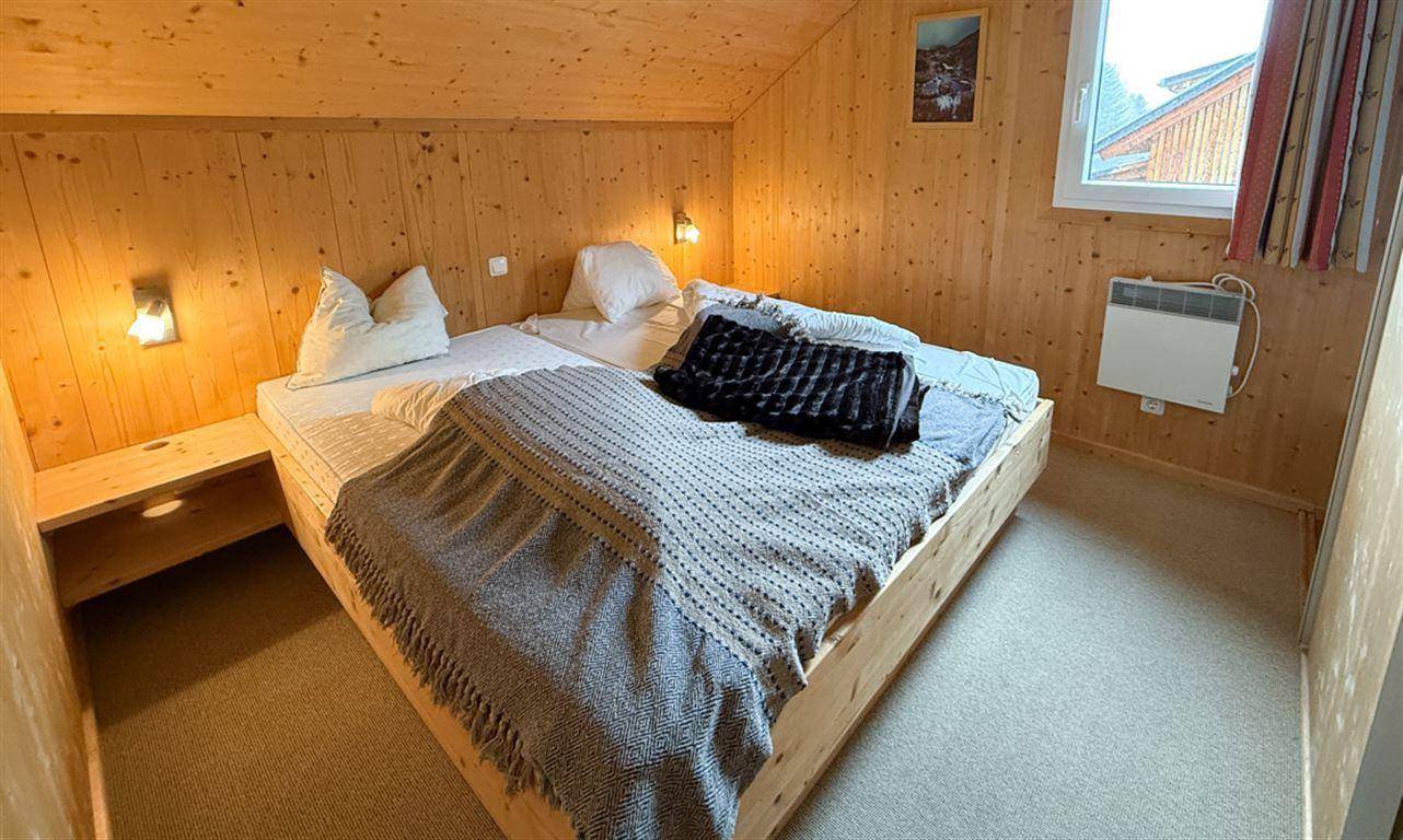 Schlafzimmer mit Holzwänden, Dachschräge und Fenster mit Blick nach draußen.