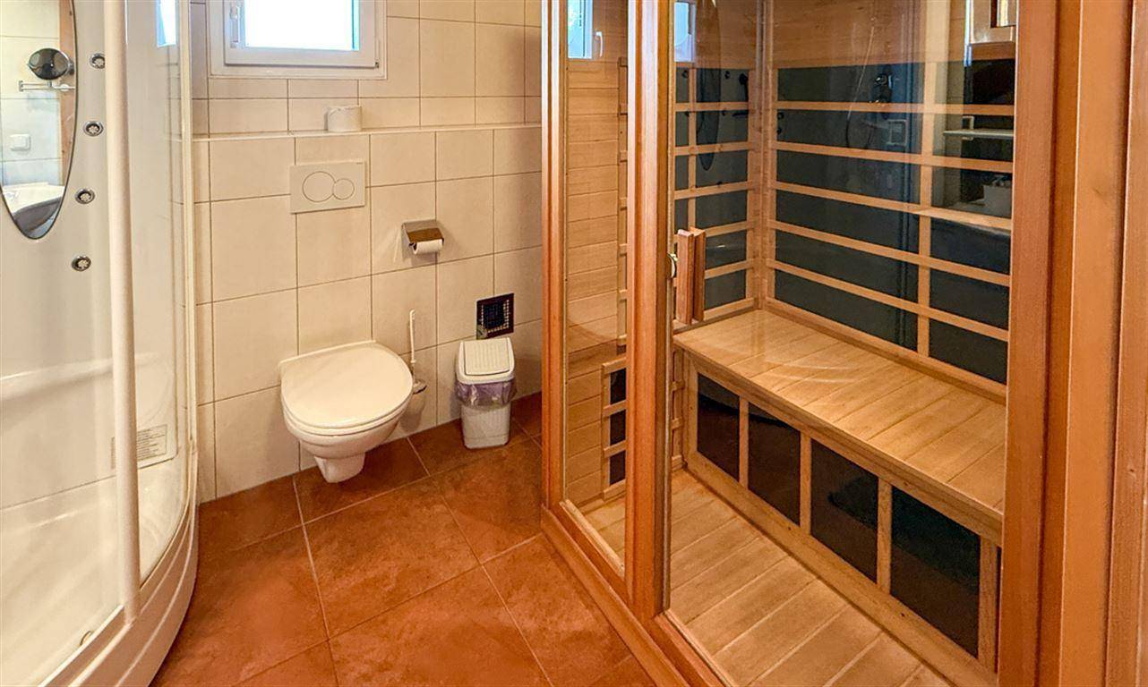 Badezimmer mit Fliesenboden, Dusche und integrierter Sauna für Wellness.
