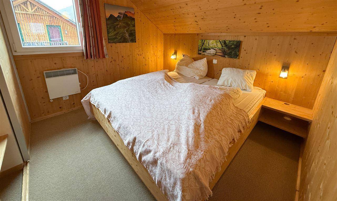 Helles Schlafzimmer mit Holzwänden, Dachschräge und Fenster für natürliches Licht.