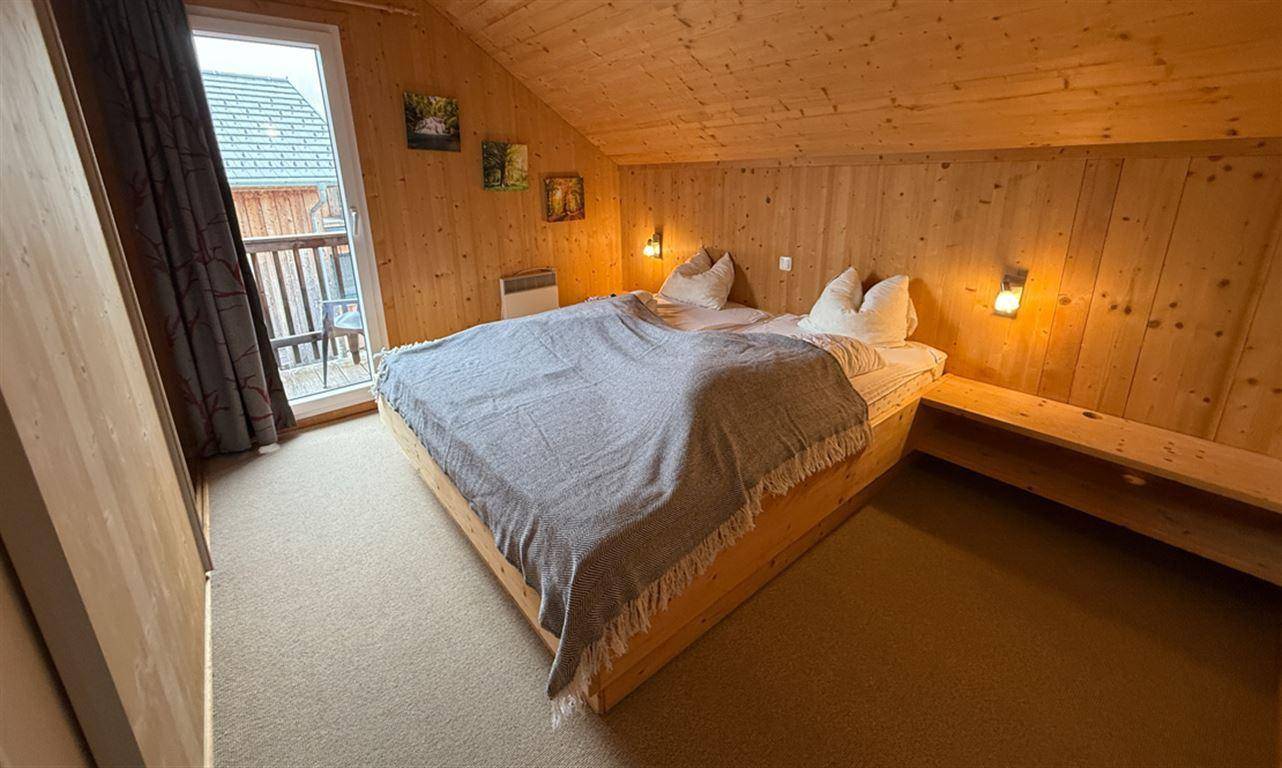 Gemütliches Schlafzimmer mit Holzeinrichtung, Dachschräge und Balkonzugang.