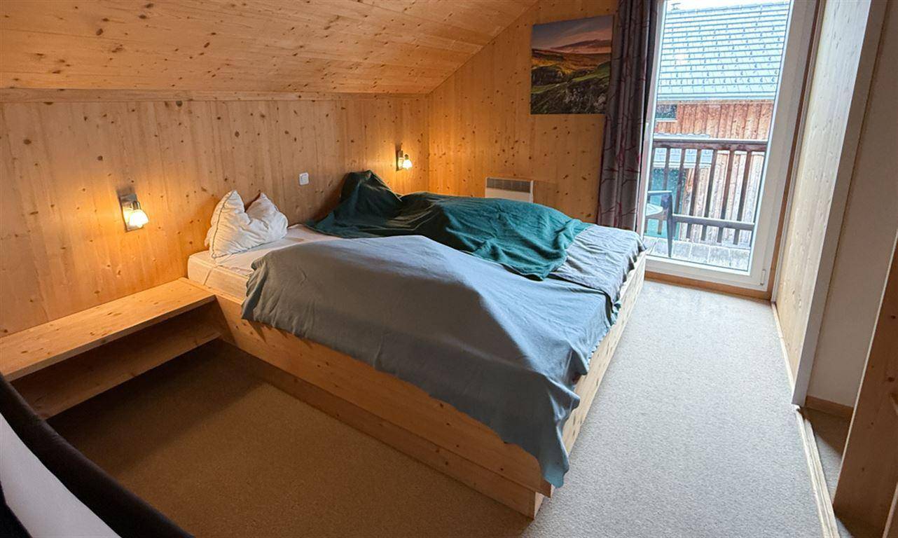 Schlafzimmer mit Holzwänden, Dachschräge und direktem Zugang zum Balkon.