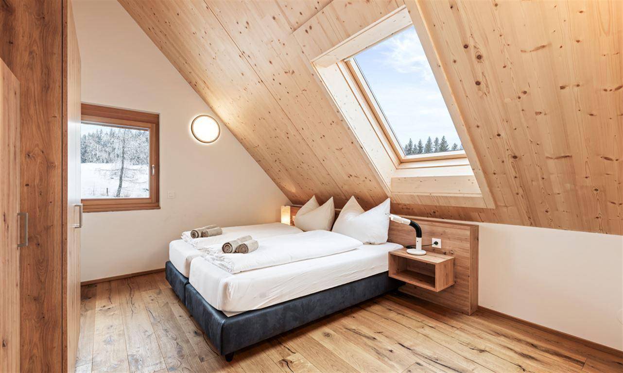 Helles Schlafzimmer mit Doppelbett, Holzboden, Dachfenster und Blick ins Grüne.