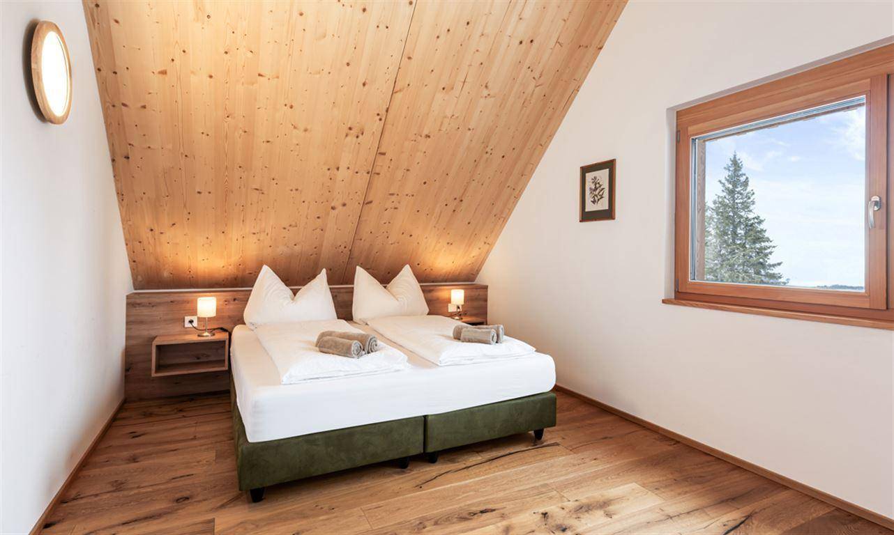 Schlafzimmer mit Holzboden, Holzwänden und Fenster mit Blick auf die Natur.