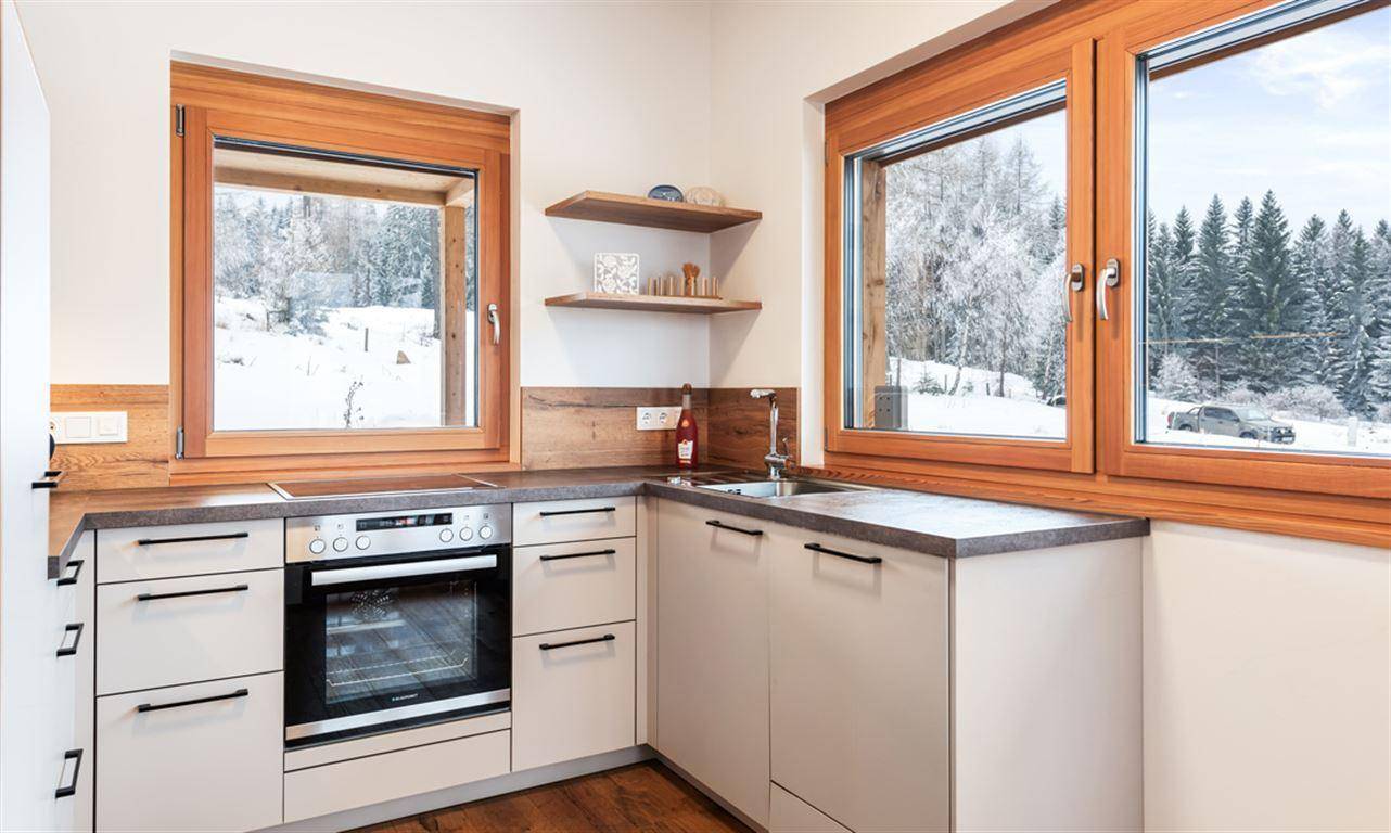 Helle Küche mit Arbeitsplatte, Kochfeld, Backofen und Blick auf die verschneite Landschaft.