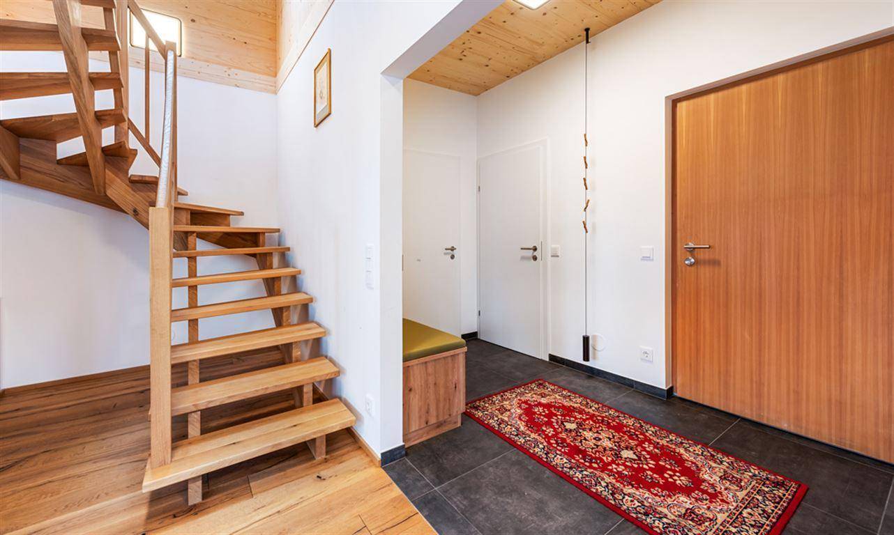 Eingangsbereich mit Holztreppe, Fliesenboden und einer praktischen Sitzbank.