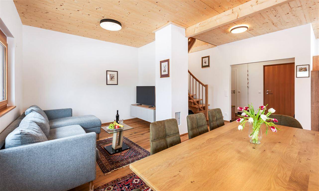 Offener Wohn- und Essbereich mit Holzdecke, bequemer Couch, Esstisch und Treppe.