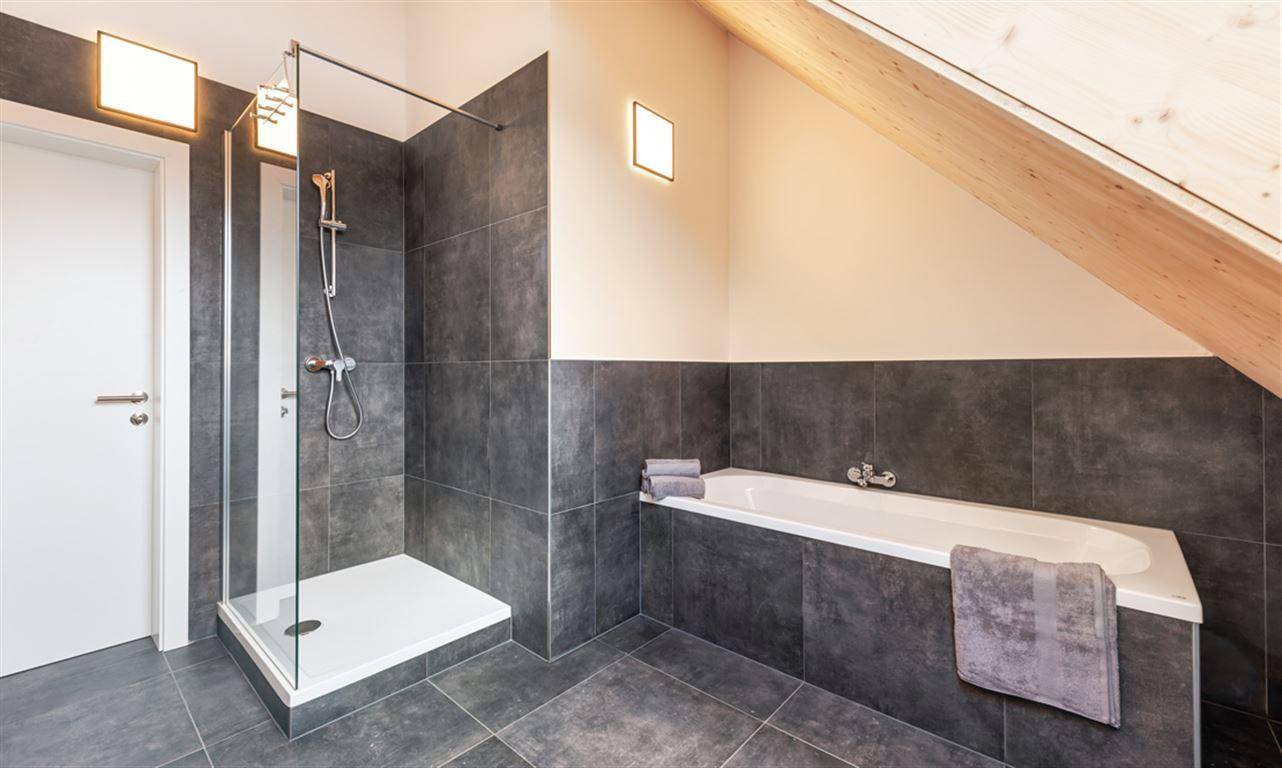 Modernes Badezimmer mit Dusche, Badewanne und eleganten dunklen Fliesen.
