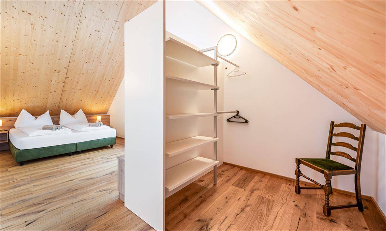 Schlafzimmer mit offenem Kleiderschrank, Holzboden und charakteristischer Dachschräge.