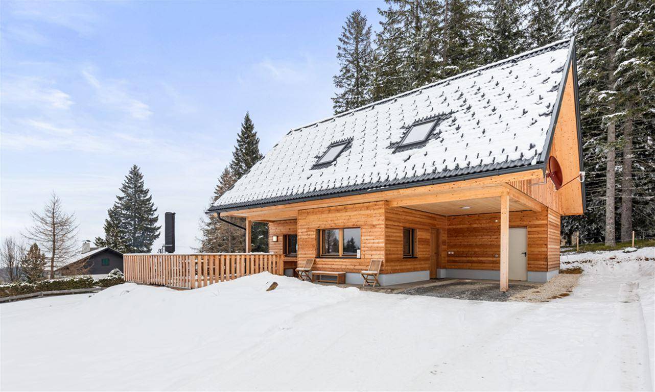 Rückseite des Holzhauses im Winter mit Carport und verschneiter Landschaft.