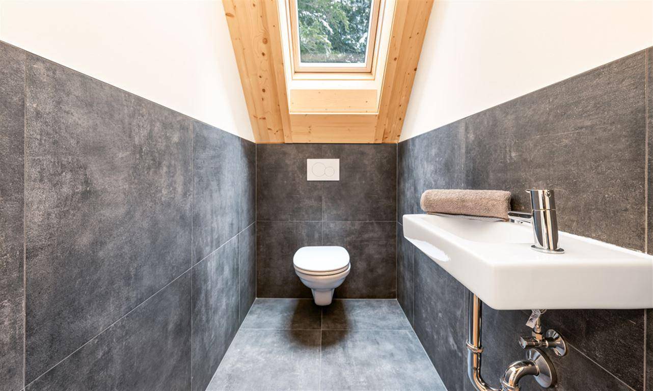 Separate Toilette mit Waschbecken, dunklen Fliesen und Dachfenster.