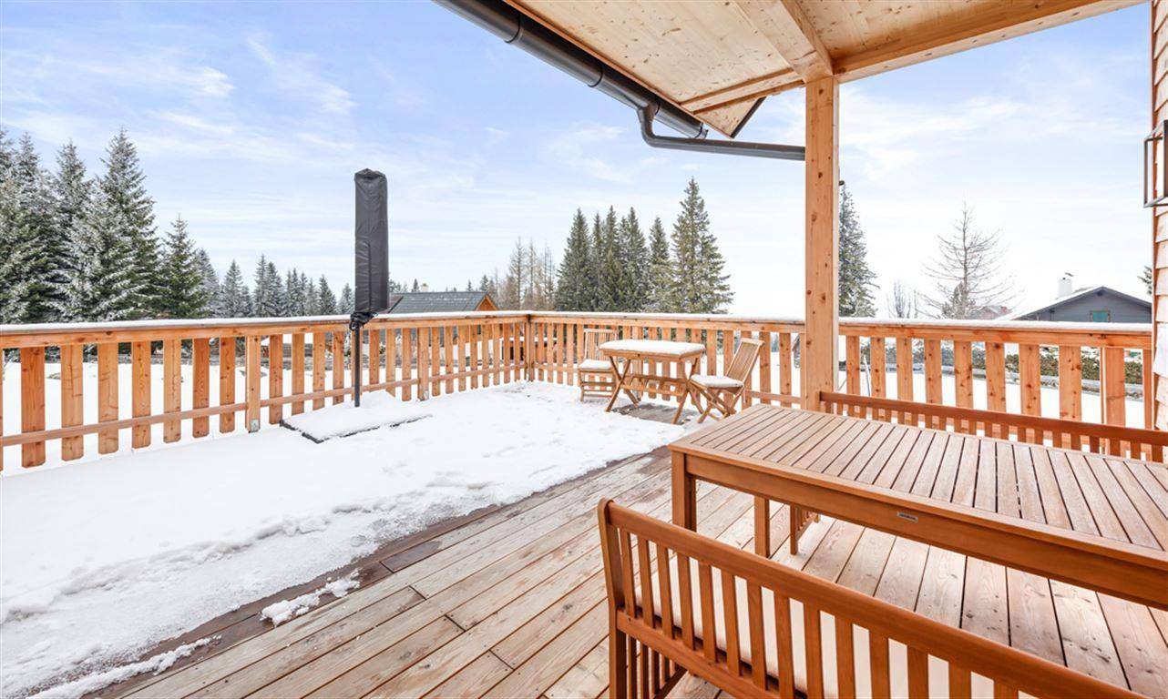 Verschneite Holzterrasse mit Outdoor-Möbeln und weitem Blick auf die Winterlandschaft.