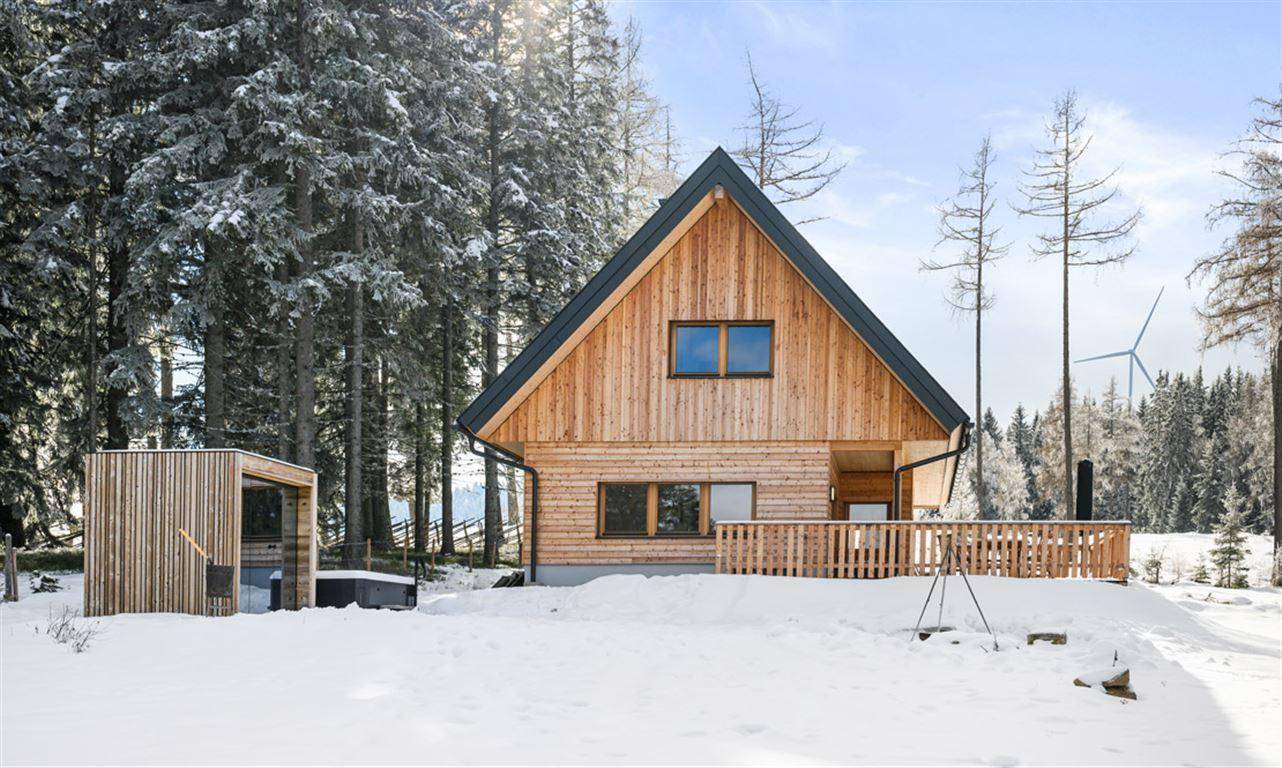Charmantes Holzhaus im Winter mit verschneiter Umgebung und Wald im Hintergrund.