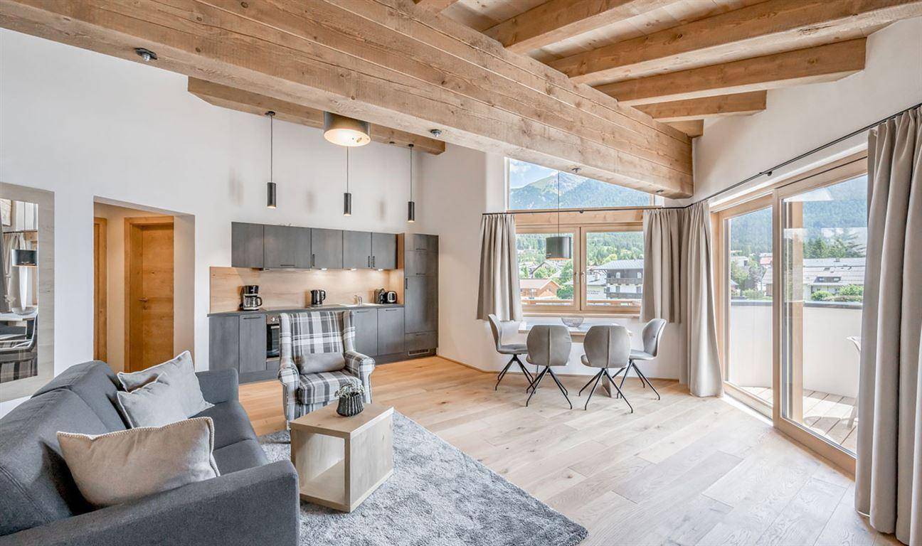 Heller Wohn-Essbereich mit offener Küche, Holzbalken und großzügigen Fenstern mit Bergblick.