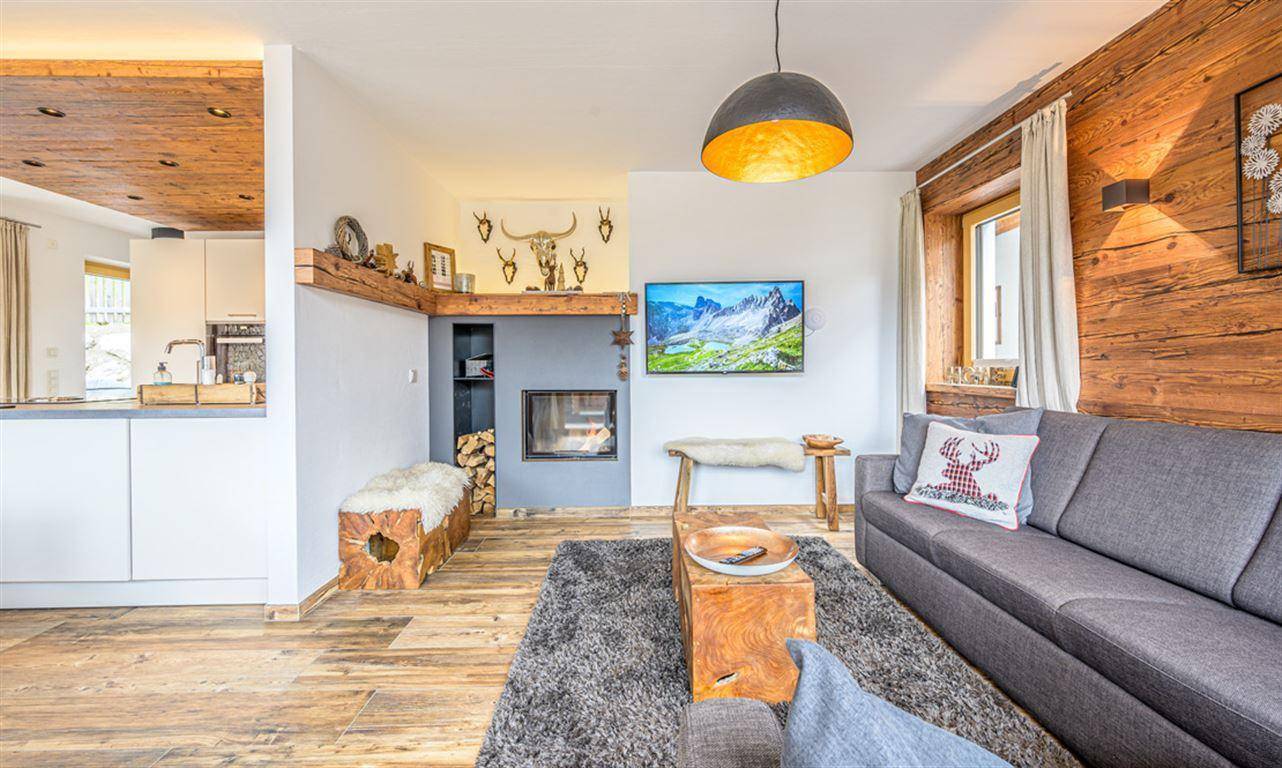 Heller Wohnbereich mit offener Küche, Kamin und Holzwand, perfekt für gesellige Stunden.