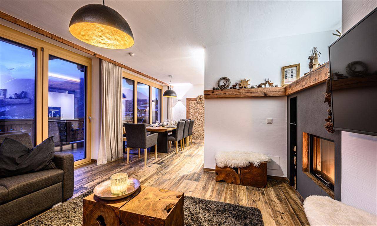 Geräumiger Wohn-Essbereich mit Kamin, Holzboden und Zugang zu einem Balkon mit Bergblick.