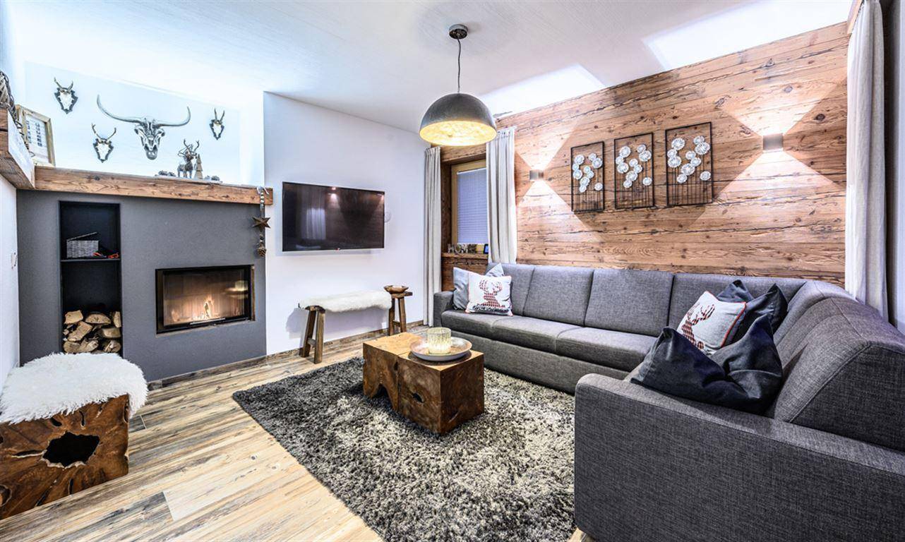Gemütliches Wohnzimmer im alpinen Stil mit Holzwand, Kamin und bequemer Sitzecke.