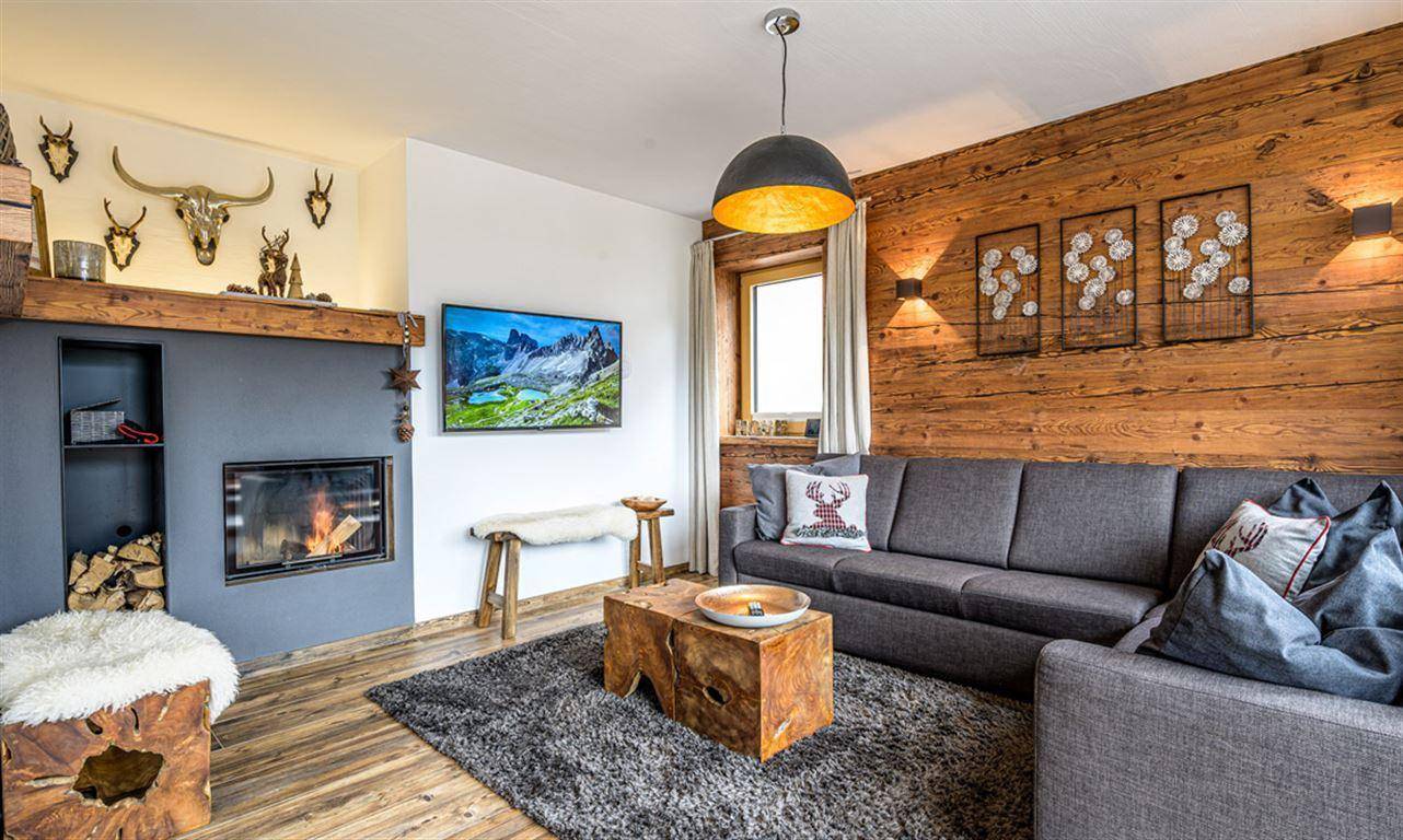Helles Wohnzimmer mit Kamin, Holzwand und Blick auf die Natur, ideal zum Entspannen.