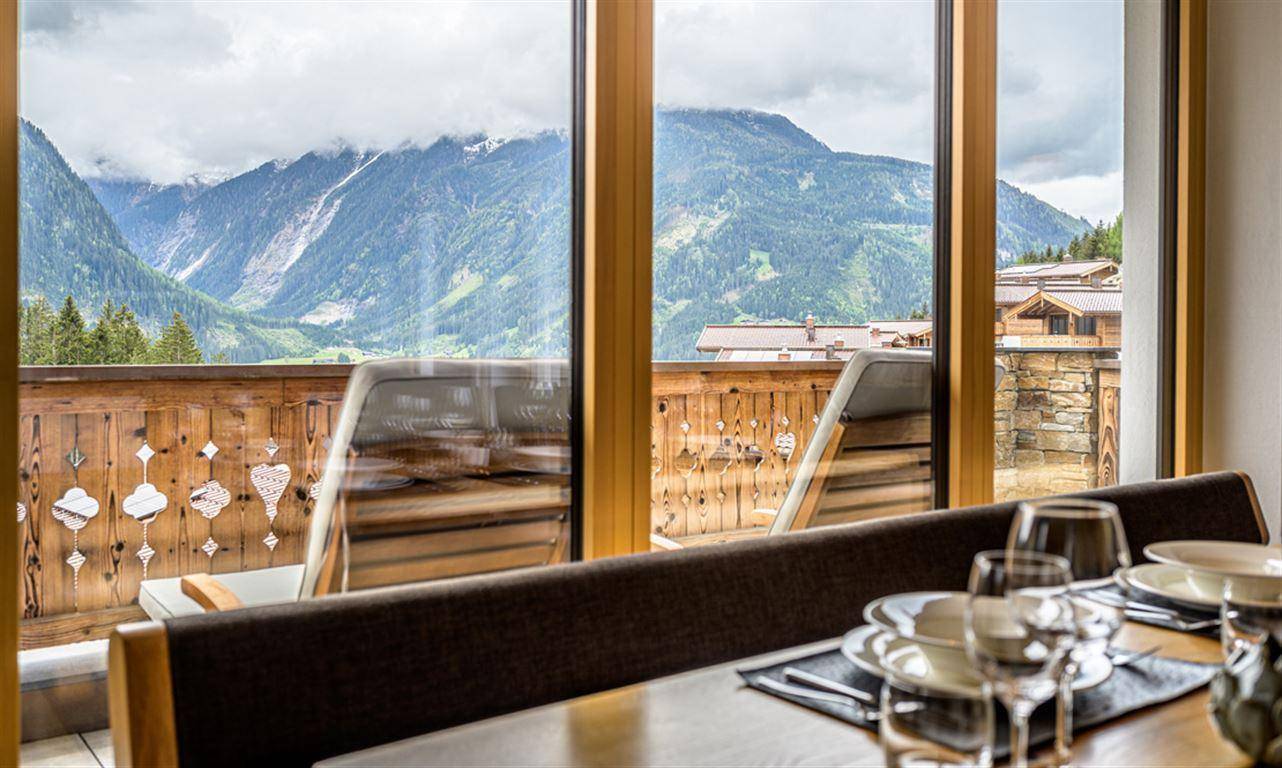 Essbereich mit Bergblick durch große Fenster, gemütliche Sitzbank und gedeckter Tisch.