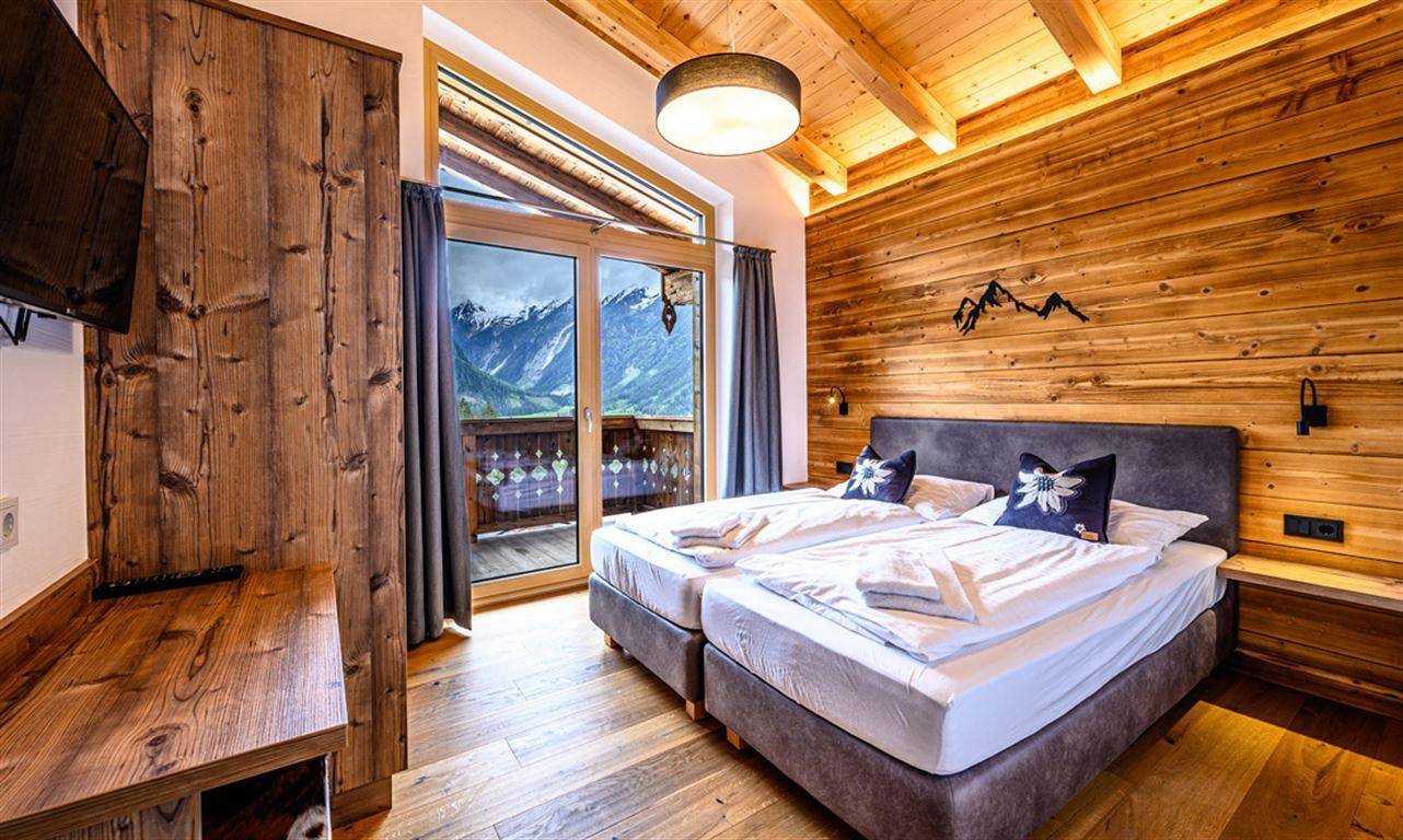 Schlafzimmer mit Holzwand, Doppelbett und Balkonzugang, bietet einen herrlichen Bergblick.
