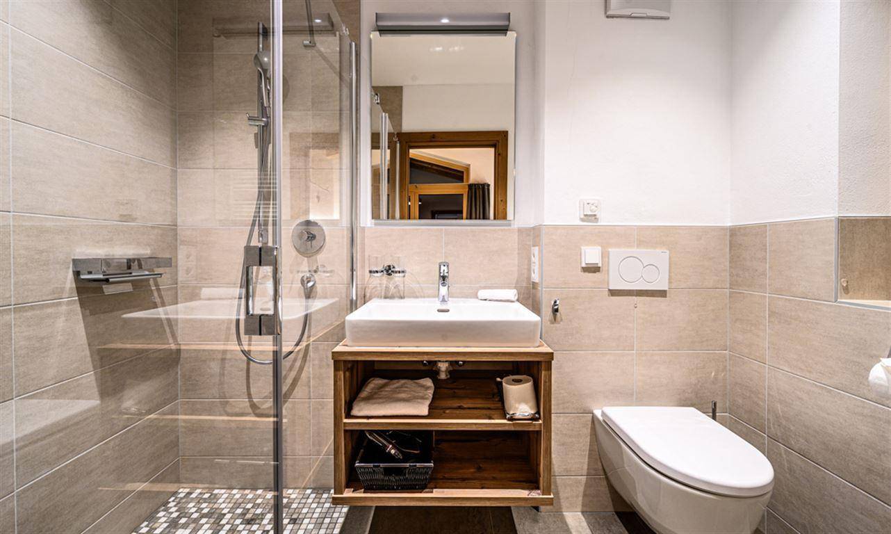 Modernes Badezimmer mit begehbarer Dusche, Wand-WC und Waschbecken mit Holzunterschrank.