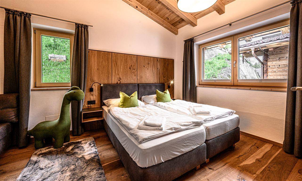 Helles Schlafzimmer mit Holzbalkendecke, Doppelbett und Fenstern mit Blick ins Grüne.