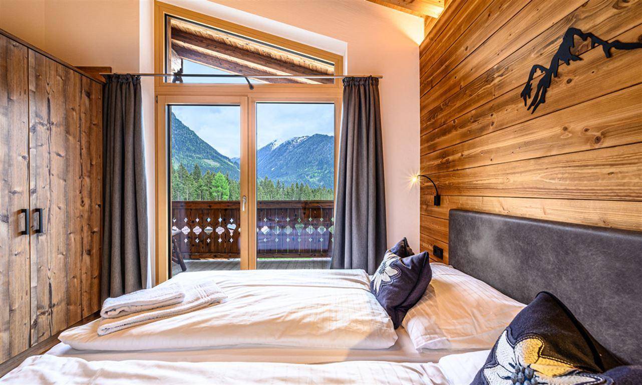Komfortables Schlafzimmer mit Doppelbett, Holzwand und großen Fenstern mit Bergblick.