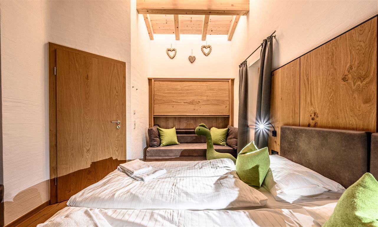 Gemütliches Schlafzimmer mit Holzbalkendecke, Doppelbett und einem kleinen Sofa.