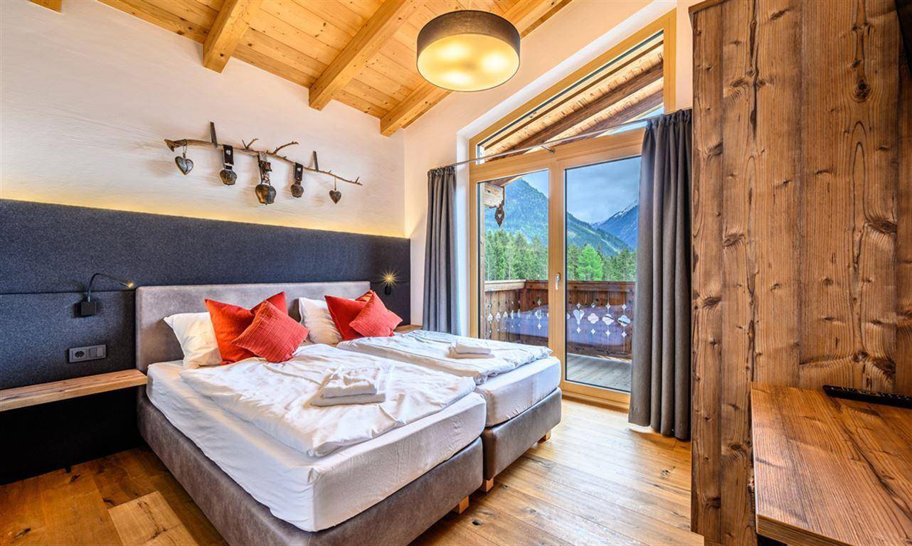 Schlafzimmer im alpinen Stil mit Holzbalkendecke, Doppelbett und Zugang zum Balkon.