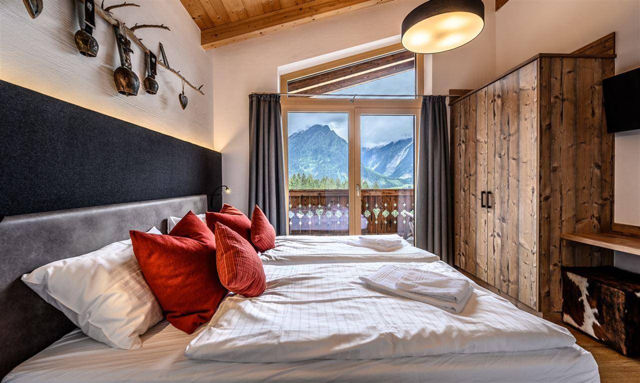 Gemütliches Schlafzimmer mit Doppelbett, Holzbalkendecke und Bergblick durch große Fenster.