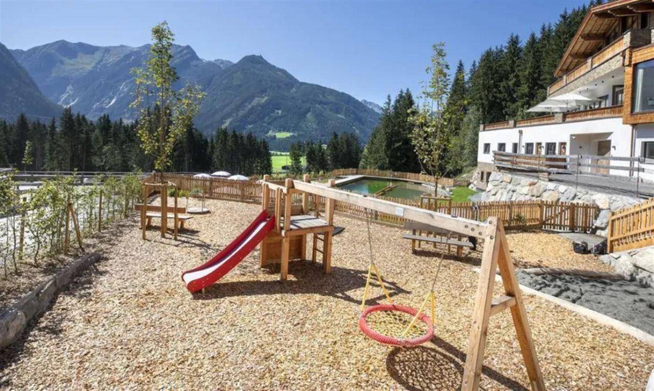 Kinderspielplatz mit Rutsche und Schaukeln, umgeben von Natur und Bergblick.