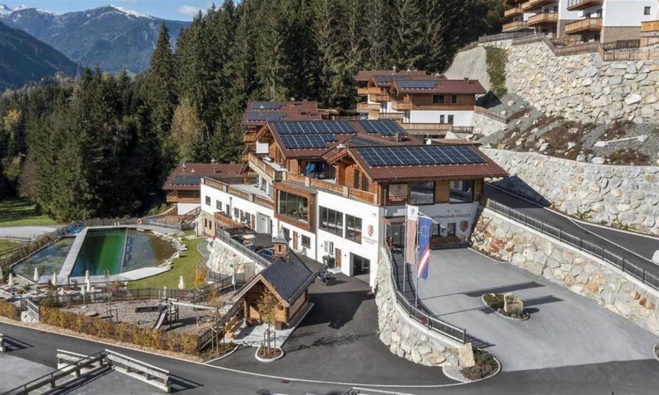 Ferienanlage in den Bergen mit Pool, Spielplatz und Photovoltaikanlage auf den Dächern.
