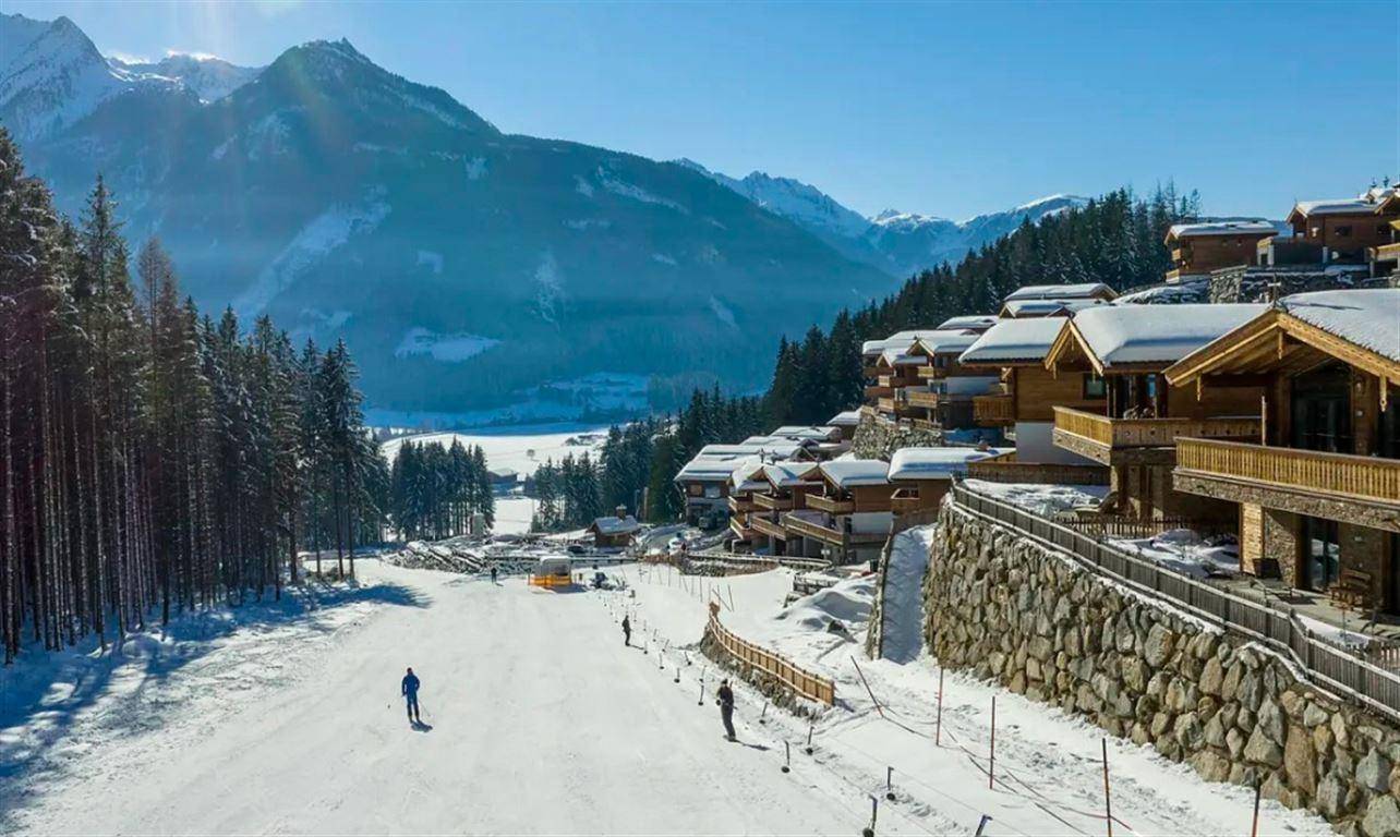 Panoramablick auf moderne Holzchalets in einer verschneiten Berglandschaft mit Skipiste.