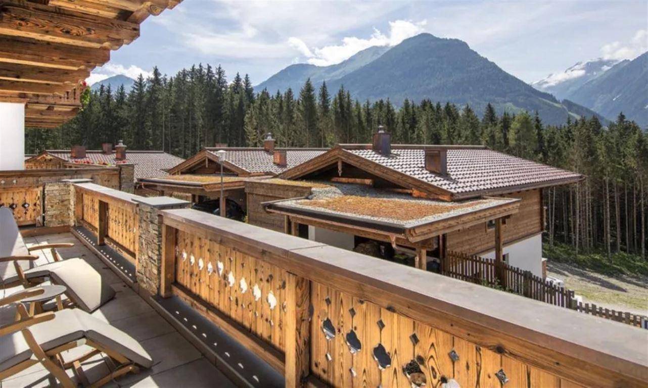 Geräumiger Balkon mit Holzgeländer und Blick auf die bewaldeten Berge und weitere Chalets.