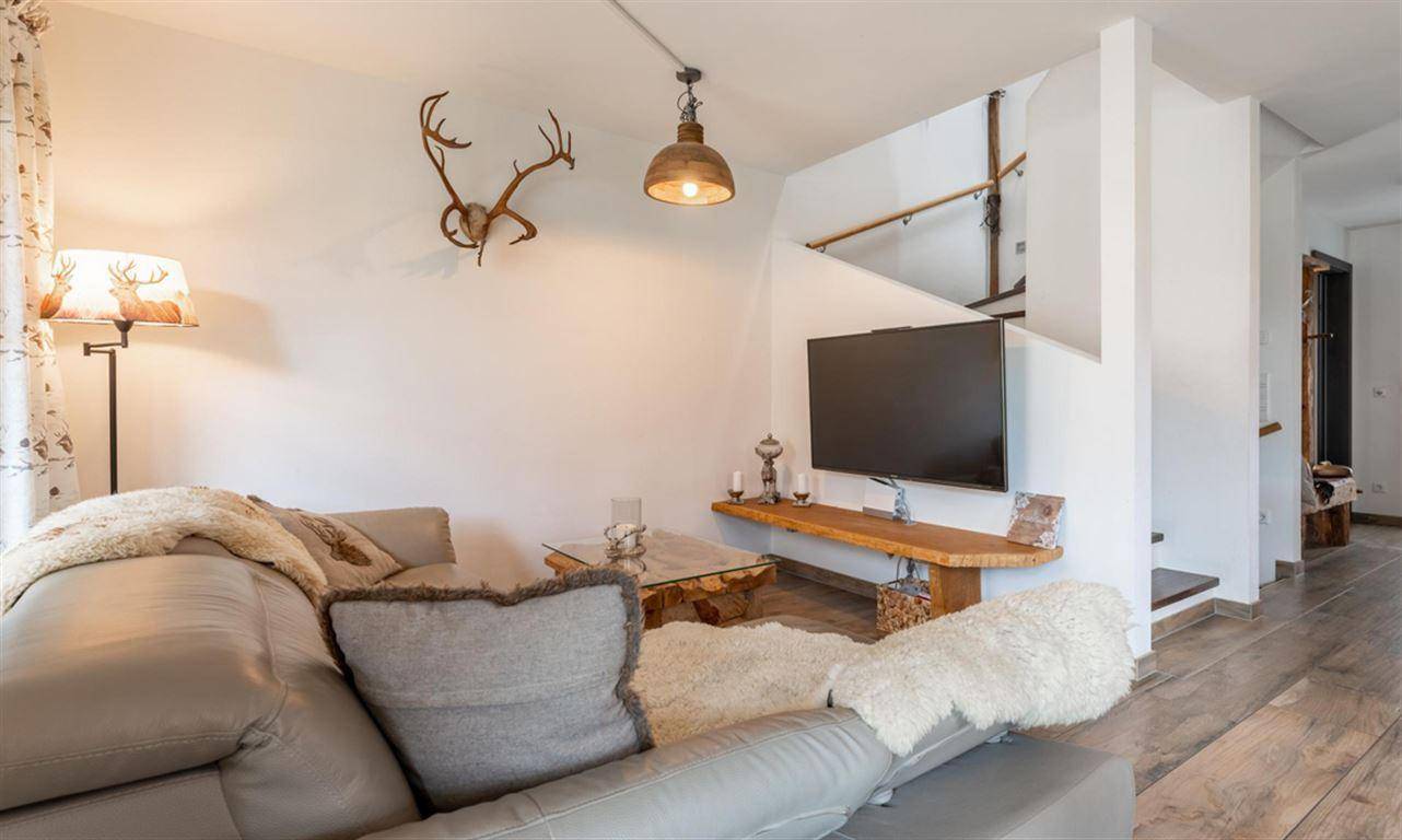 Gemütliches Wohnzimmer mit Sofa, Fernseher und rustikalen Hirschgeweih-Dekorationen im Landhausstil.
