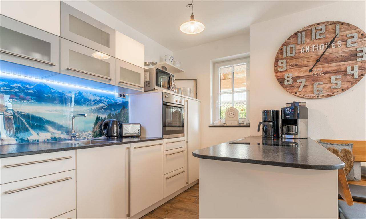 Moderne Einbauküche mit weißen Schränken, dunkler Arbeitsplatte und Fenster für viel Licht.