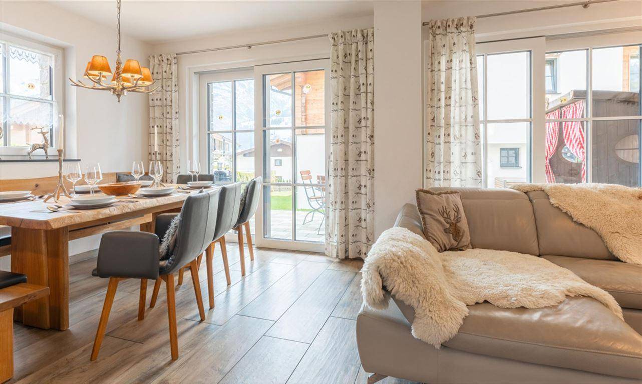 Gemütlicher Wohn-Essbereich mit Holztisch, bequemer Couch und großen Fenstern zur Terrasse.