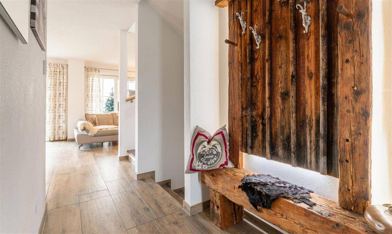 Eingangsbereich mit rustikaler Holzbank, Garderobe und Fliesenboden im alpinen Stil.