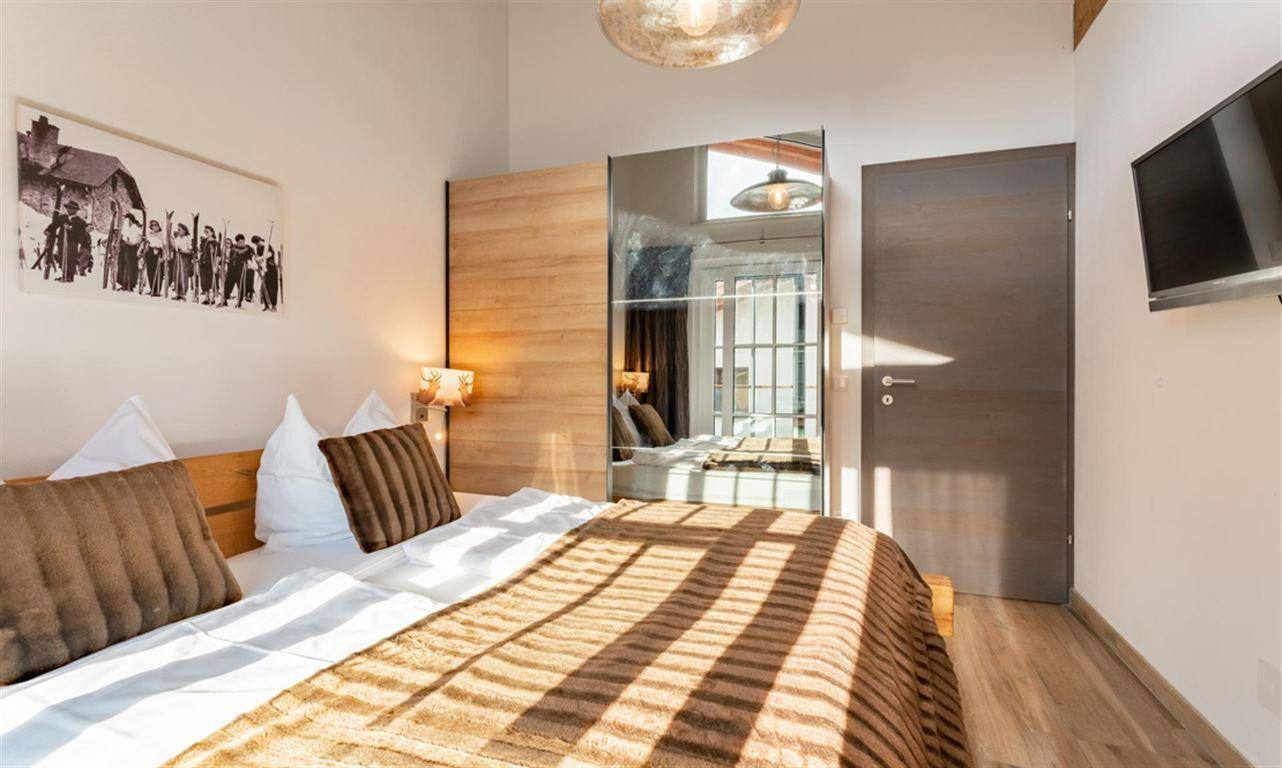 Helles Schlafzimmer mit Doppelbett, Spiegelschrank und Holzbalkendecke für ein offenes Raumgefühl.
