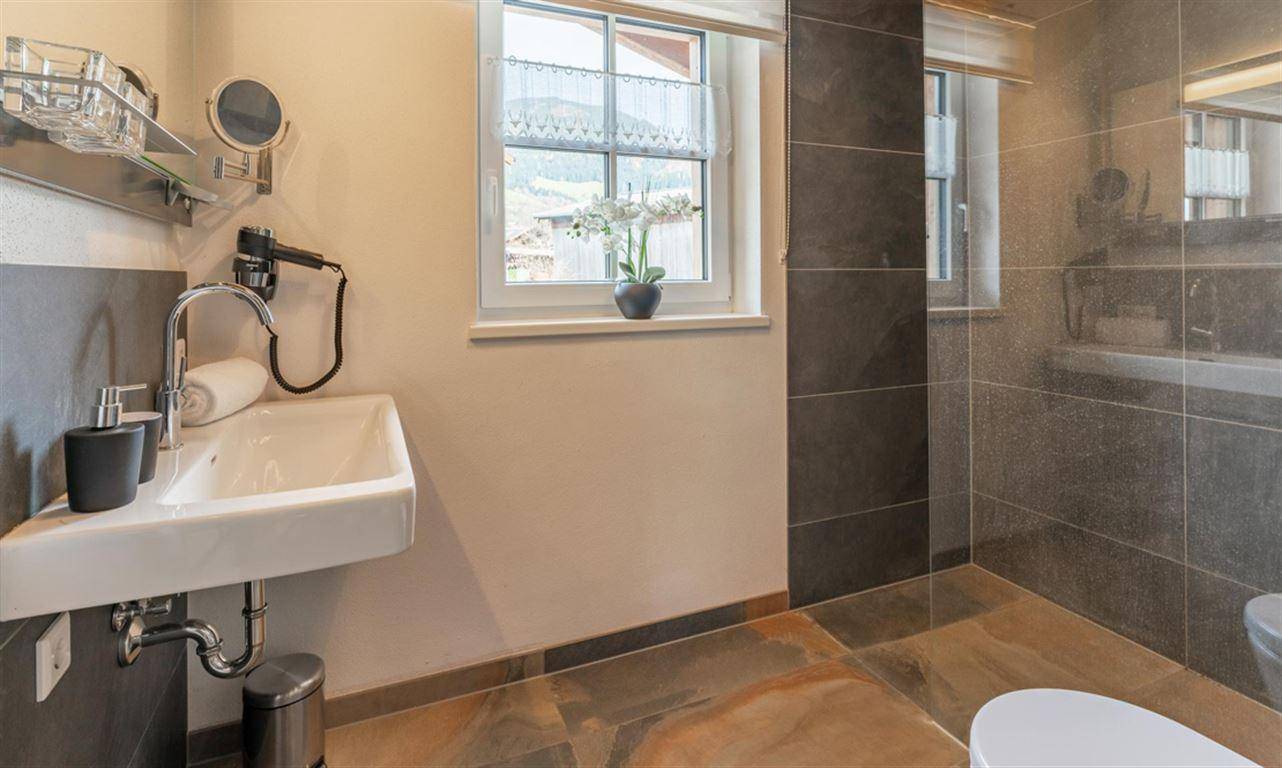Modernes Badezimmer mit Waschbecken, Dusche und Fenster für natürliche Belüftung.