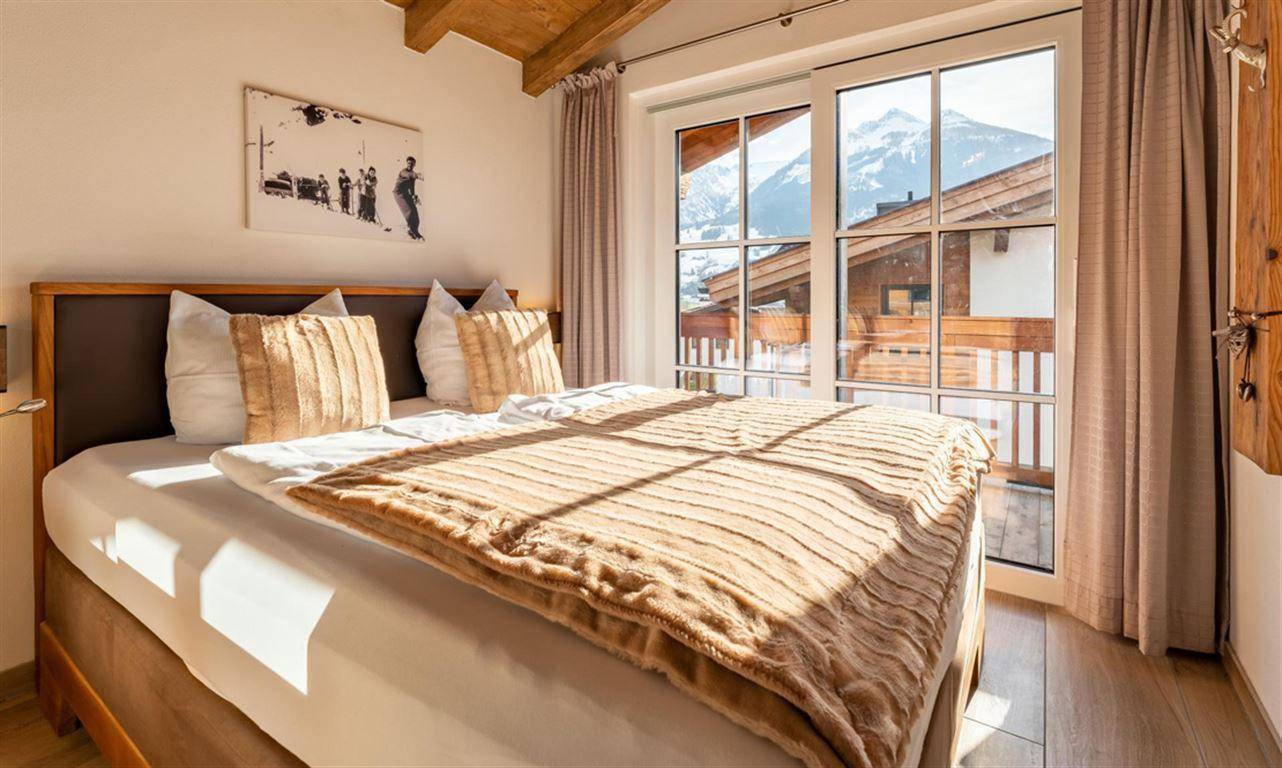 Schlafzimmer mit Doppelbett, Holzbalkendecke und Zugang zum Balkon mit Bergblick.