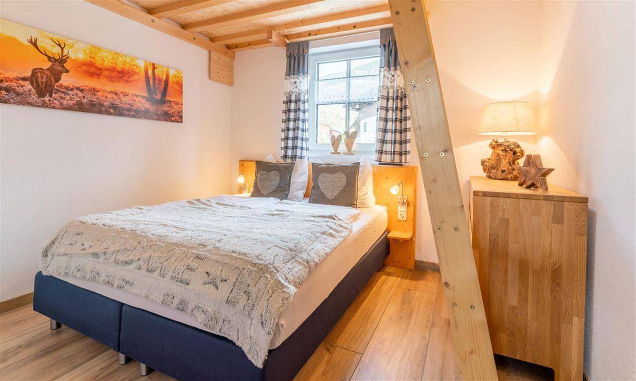 Schlafzimmer mit Doppelbett, Holzmöbeln und Leiter zu einem zusätzlichen Schlafbereich.